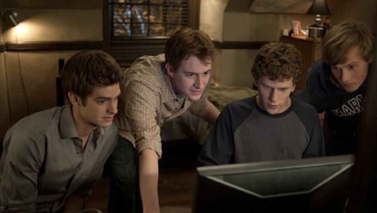 The four creators of Facebook huddled behind a computer.